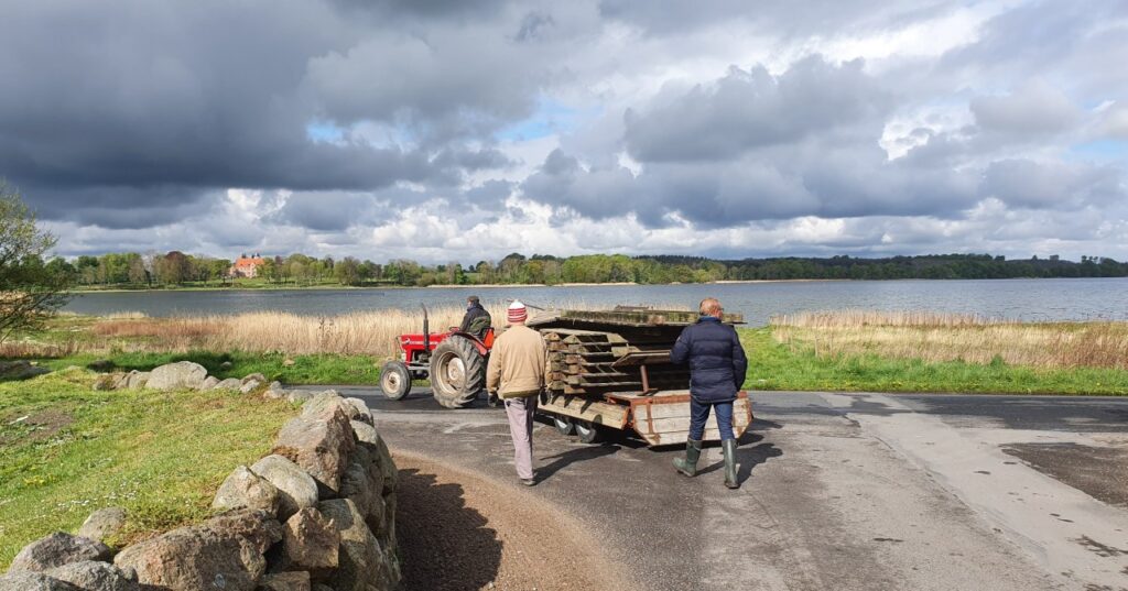 Broelementer på vej til brofæstet på vogn efter lille traktor